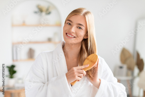 Blonde woman smiling at camera brushing her long hair indoor