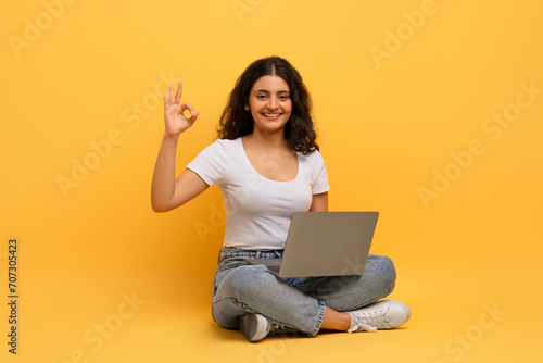 Positive young indian woman with laptop showing okay gesture © Prostock-studio