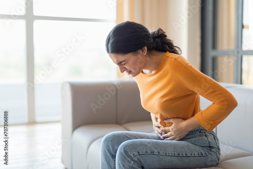 Stressed young indian woman touching her stomach, suffering acute abdominal pain photo