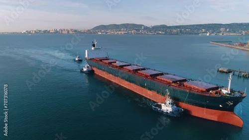 Huge cargo ship, towed by small towing boats, enters the port to load grain crops into dry holds and send the grain for export to Europe photo