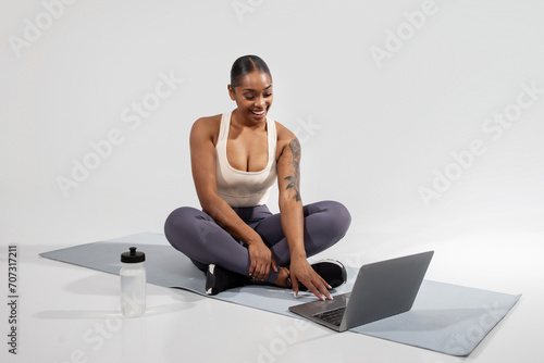 African American fitness lady browsing online workout on laptop, studio