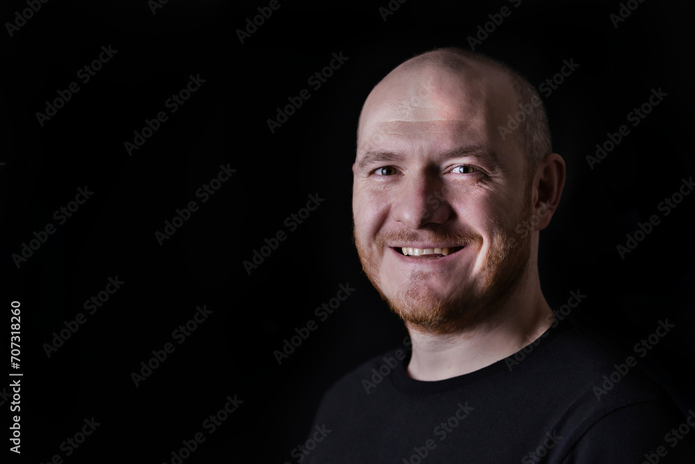 Portrait of smiling adult bald man on black background. Close up portrait of pleased white man in low key.