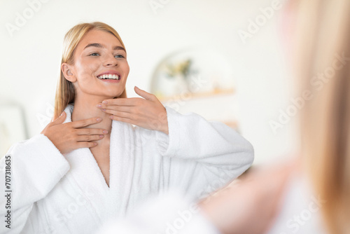 woman applies moisturizer to neck and face skin in bathroom