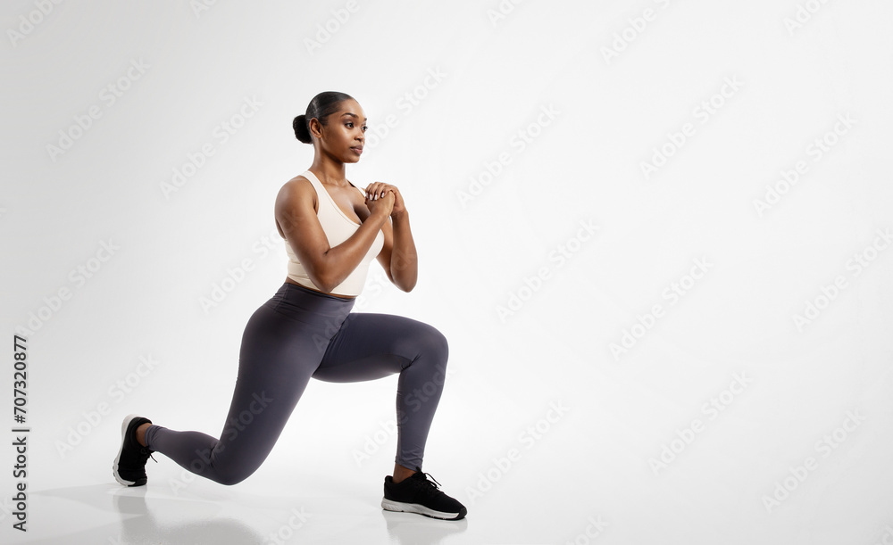 African American fitness woman stretching legs performing forward lunges, studio