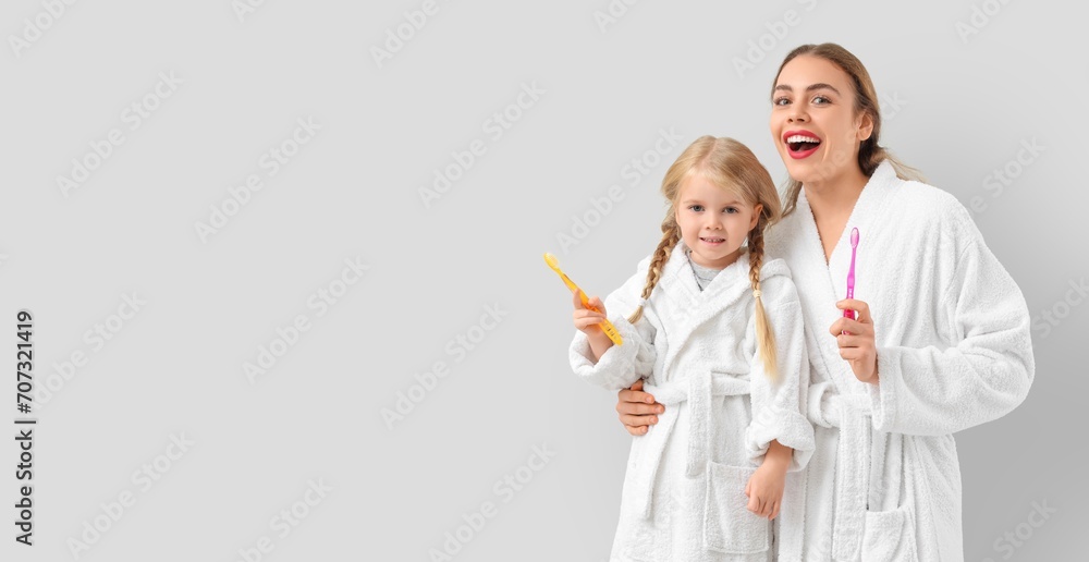 Young mother and her little daughter in bathrobes and with toothbrushes on light background with space for text Young mother and her little daughter in bathrobes and with toothbrushes on light background with space for text