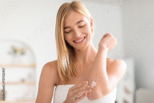 Photography Attractive blonde woman applies moisturizer on elbow in bathroom