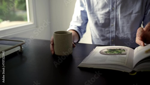 Man looking through cook book whilst holding coffee mug