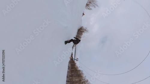 A snowboarder films himself on a 360 camera, snowboarding, ski resort, snowboarder in motion, snowboarder in black clothes, vertical shooting of a snowboarder, vertical shooting photo