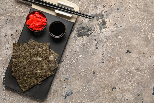 Board with nori sheets, ginger and soy sauce on grunge background photo