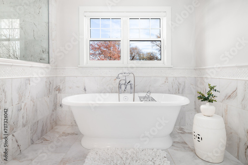 A freestanding bathtub with a chrome faucet surrounded by marble tiles on the floor and walls. No brands or labels.