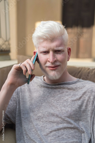 Portrait of a young albino man sitting down talking on the phone