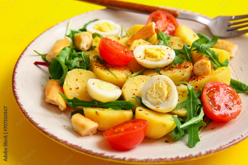 Plate of tasty potato salad with eggs and tomatoes on yellow background, closeup