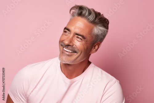 Portrait of handsome mature man smiling and looking at camera against pink background
