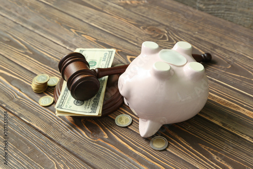 Piggy bank with judge gavel and money on brown wooden background. Concept of bankruptcy photo