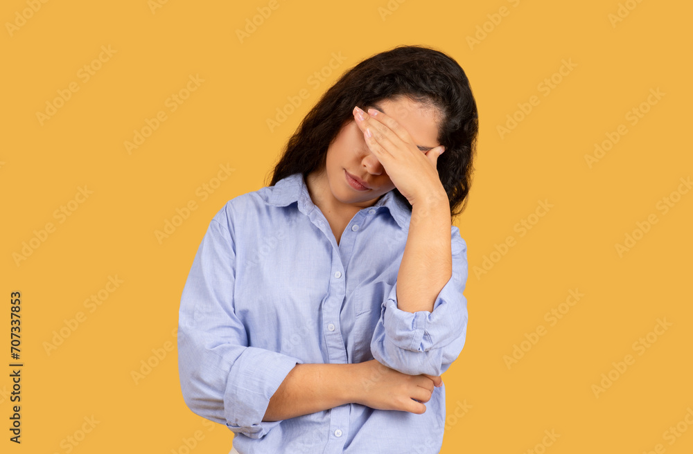 Stressed young woman in a light blue shirt holding her forehead in frustration or headache Stressed young woman in a light blue shirt holding her forehead in frustration or headache