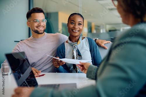 Happy multiracial couple giving their documents to insurance agent during meeting in office. photo