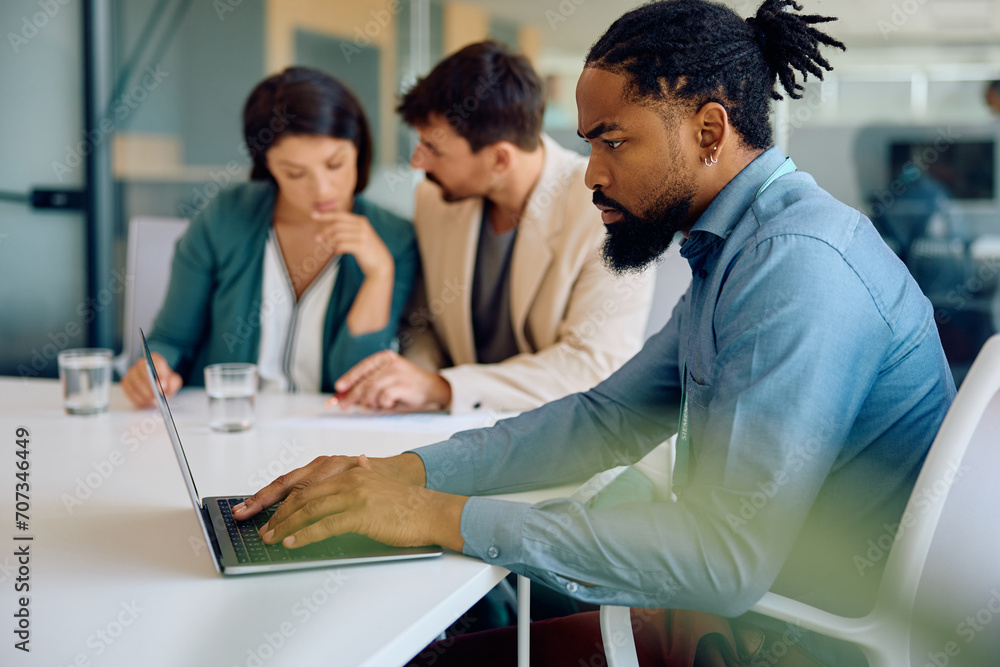 Black bank manager working on laptop during meeting with clients in office. Black bank manager working on laptop during meeting with clients in office.