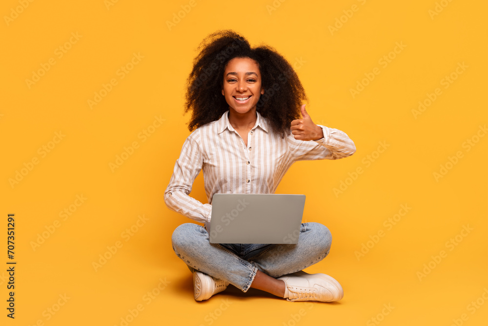 Happy black woman with laptop giving thumbs up on yellow background Happy black woman with laptop giving thumbs up on yellow background