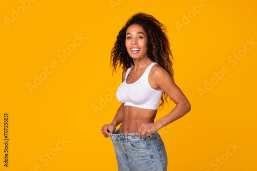 Happy african american lady pulling too big jeans waist, studio photo
