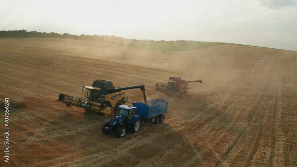 BERLIN , GERMANY - JULY 15 2023: Harvester machine loads wheat grains into tractor trailer on dusty plantation aerial view. Combine reaper unloads gathered cereal crop at sunset BERLIN , GERMANY - JULY 15 2023: Harvester machine loads wheat grains into tractor trailer on dusty plantation aerial view. Combine reaper unloads gathered cereal crop at sunset
