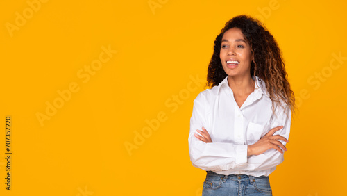 Black woman confidently posing with hands crossed against yellow background