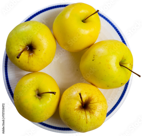 Juicy golden delicious apples are on plate. Yellow fruits shine in rays of sun and lighting. Isolated over white background