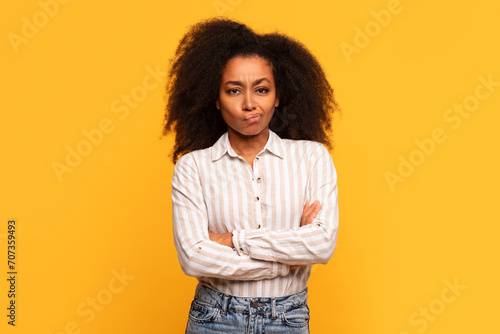 Skeptical black lady with arms crossed on yellow background photo
