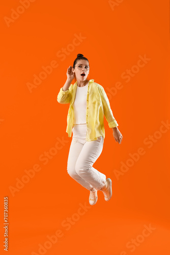 Jumping young gossip woman trying to hear something on orange background photo