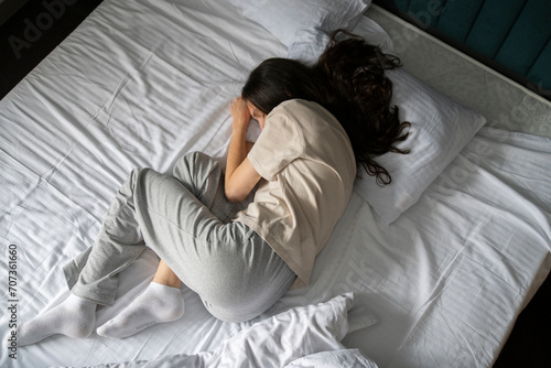 A woman is captured taking a nap, curled up in a bad wrong on a white-sheeted bed, suggesting a midday or early morning rest. photo