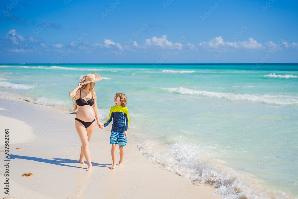 A radiant pregnant mother and her excited son share a tender moment on a serene, snow-white beach, celebrating family love amidst nature's beauty
