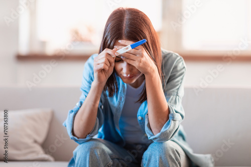 Distressed pregnant woman holding pregnancy test covering face at home photo