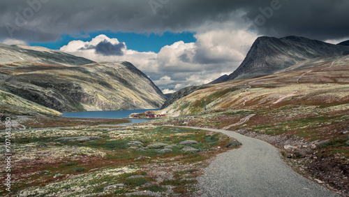 Rondane national park with footpath leading to lake Rondvassbu and hut, framed with mountains, cloudy dramatic sky, Norway. photo