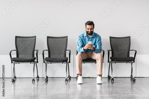Indian man using smartphone while sitting in empty waiting area photo