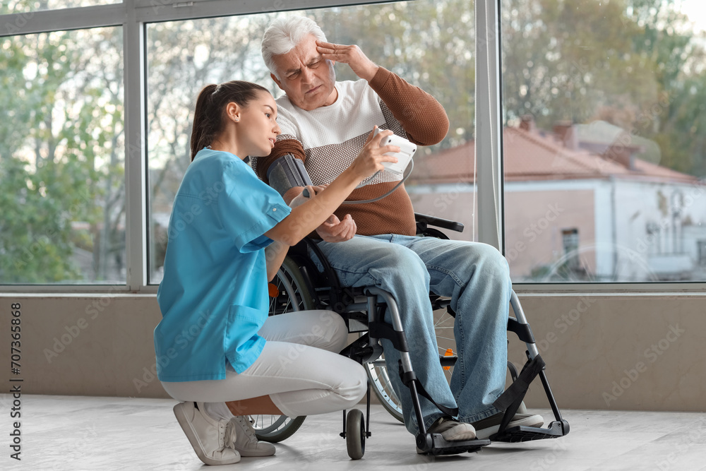 Φωτογραφία Nurse measuring blood pressure of senior man in wheelchair at hospital