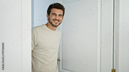 Smiling young man with a beard opening a white door inside a bright home photo