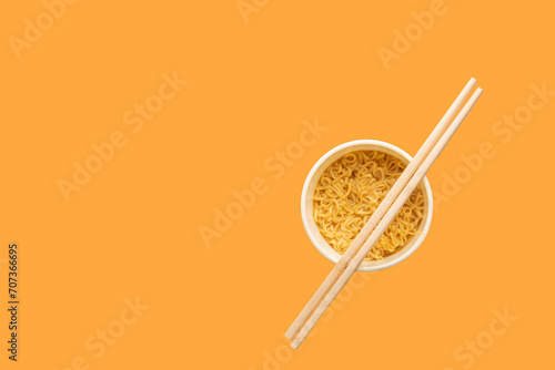 Overhead view of a bowl of instant pasta soup with a pair of chopstickson a yellow background. Lunch. Fast food concept
