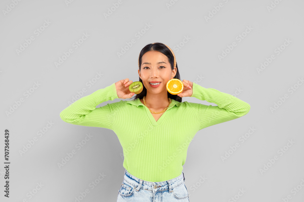 Pretty young Asian woman with orange and kiwi on lilac background Pretty young Asian woman with orange and kiwi on lilac background