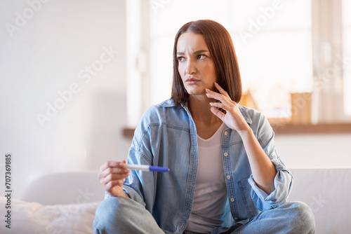 Thoughtful lady holds pregnancy test making decision sitting at home photo