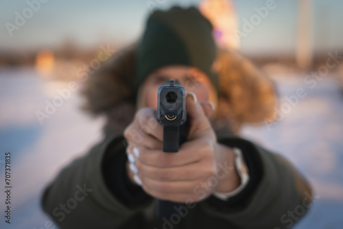 A young girl takes aim with a 9mm tactical pistol outdoors in winter. Soft focus photo.