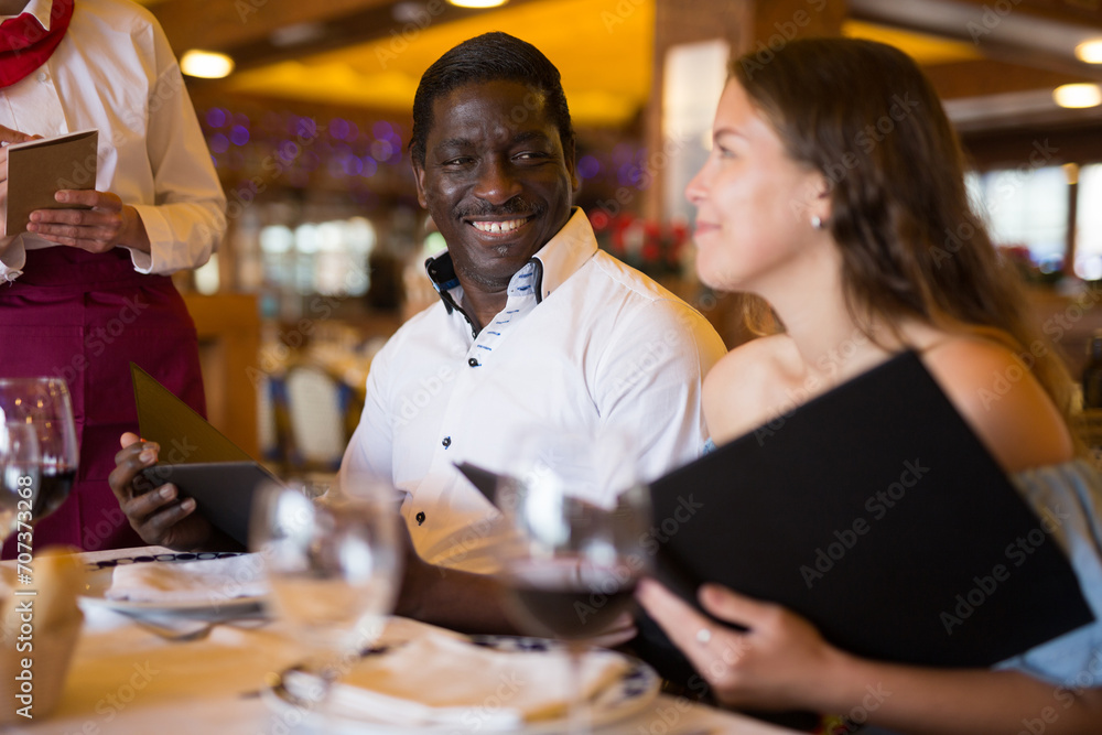 Positive female waiter writing down order from visitors in country restaurant