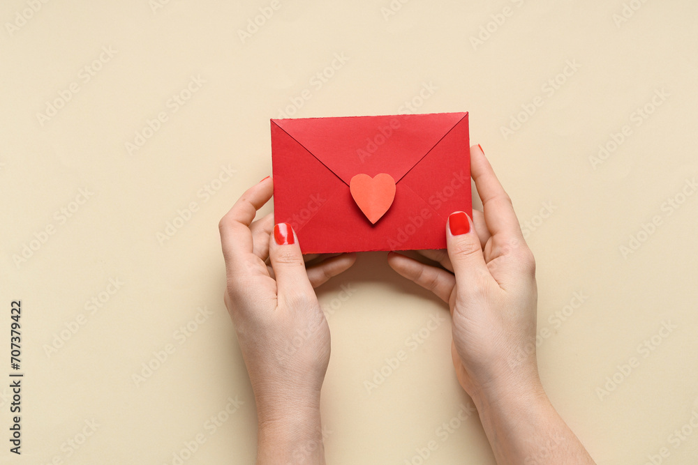 Female hands with red manicure and envelope on beige background. Valentine's Day celebration Female hands with red manicure and envelope on beige background. Valentine's Day celebration