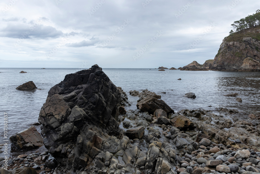 a tranquil, rugged coastal scene with jagged rock formations and a calm sea under an overcast sky