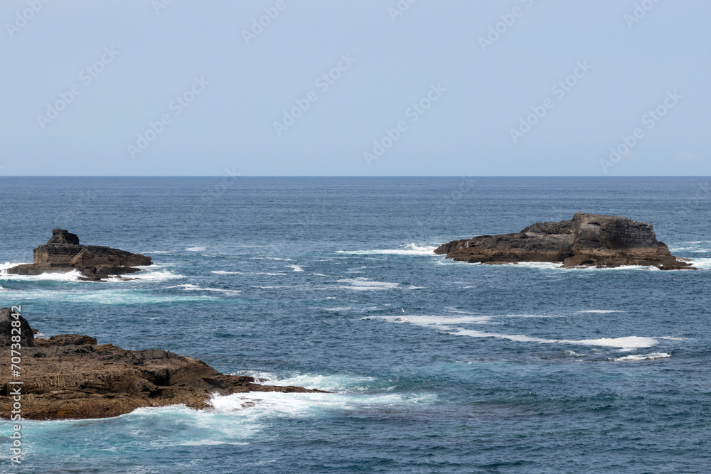 a serene yet dynamic seascape with rocky outcrops amidst turbulent ocean waves under a clear sky