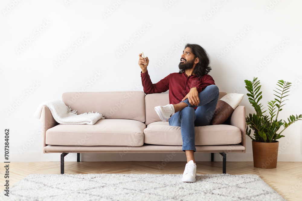 Relaxed millennial Indian man turning on AC at home