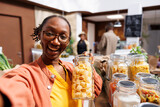 POV of a black woman wearing glasses, holding a glass container filled with pasta in a bio-food supermarket. Online marketing, organic items, vlogging, digital camera, customer filming.