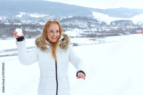 Young beautiful redhaired woman in white jacket playing snowballs beautiful frosty day. Ginger smiling young woman outside in winter day.