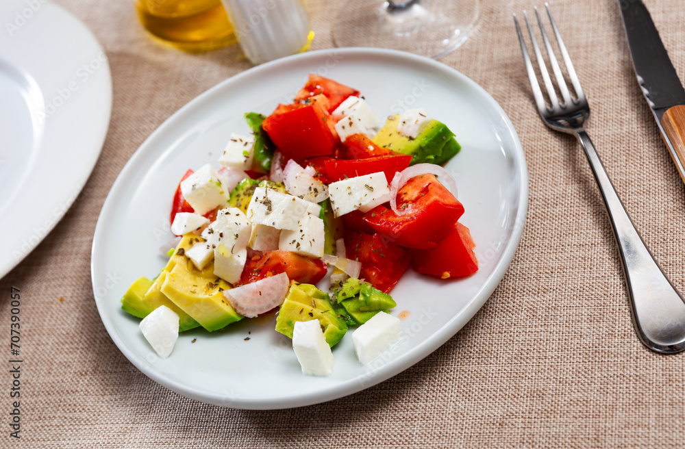 Tasty salad with avocado, tomatoes, cheese and onion is served on a plate
