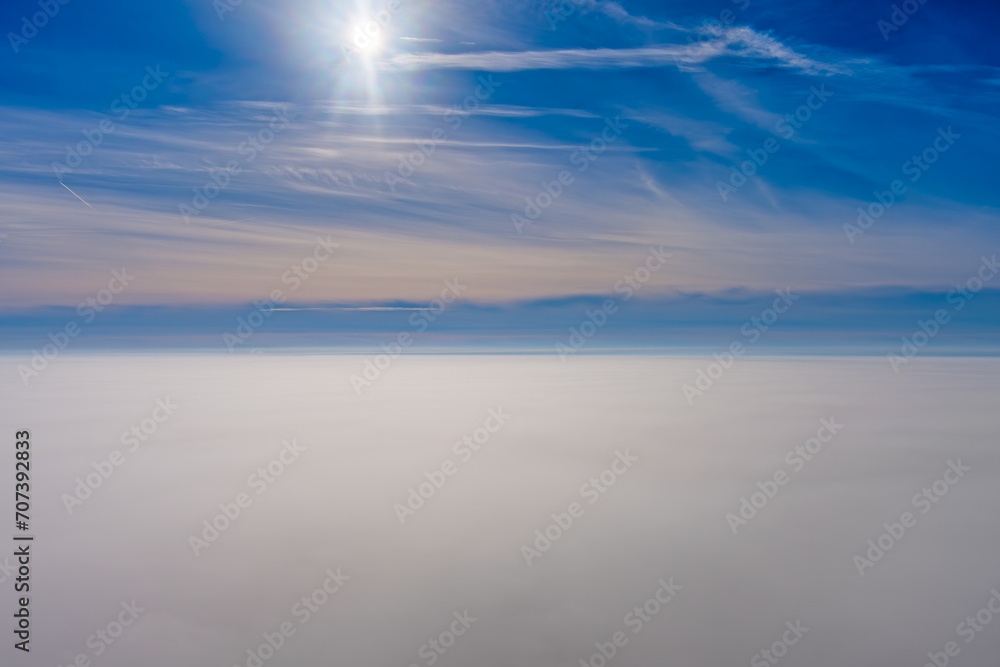 Aerial view of the sky above dense fog with a bright sun, clouds, and Airplane Jet Trails