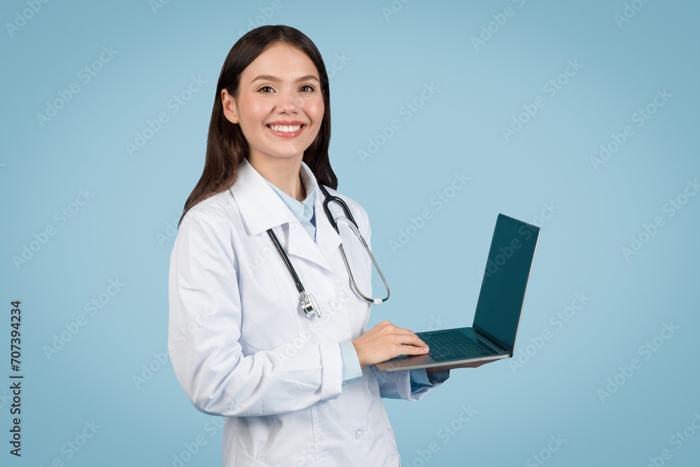 Smiling woman doctor using laptop on light blue background Smiling woman doctor using laptop on light blue background