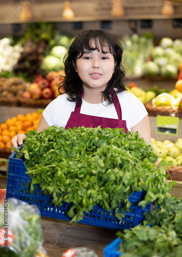 Smiling young saleswoman holding a box full of parsley at the counter in big grocery store © JackF